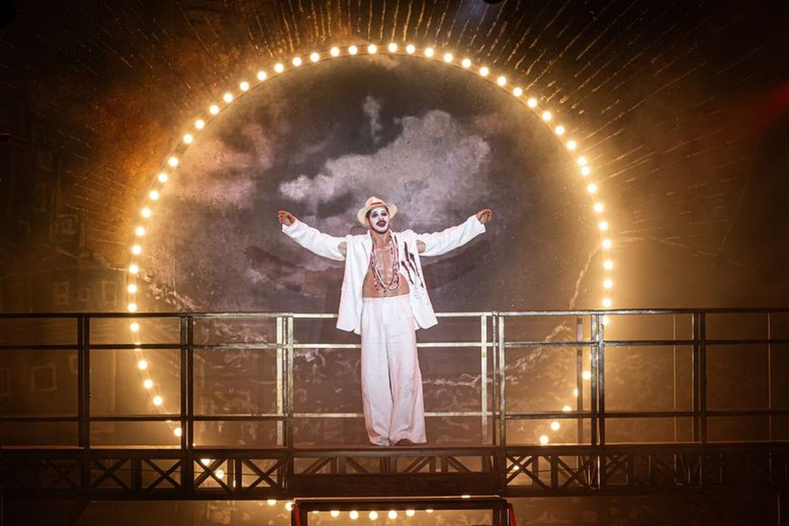 José Loreto como Max Overseas em cena, sob um arco de luzes